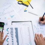 Colleagues collaborating on financial charts and graphs using mobile and paper documents in the office. — Are Air Heat Pumps