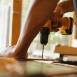 Crop anonymous male drilling timber plank with professional screwdriver on table in workshop — Cost-Effective Asbestos Survey