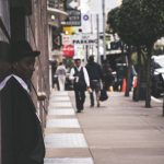 A man in a suit and hat leans against a city building, observing pedestrians. — Enhancing On-Site Efficiency with Constructio