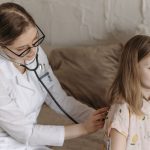A doctor with a stethoscope examining a smiling girl during a medical check-up at home. — How Digital Media Has Improved the
