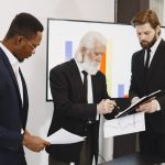 Three businessmen in suits reviewing reports and graphs during an office meeting. — How to Land a Part-Time Karaoke Assistant