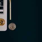 Close-up view of Bitcoin and Ethereum coins next to a laptop and pen on a black surface. — How to Navigate Volatility on Cryp