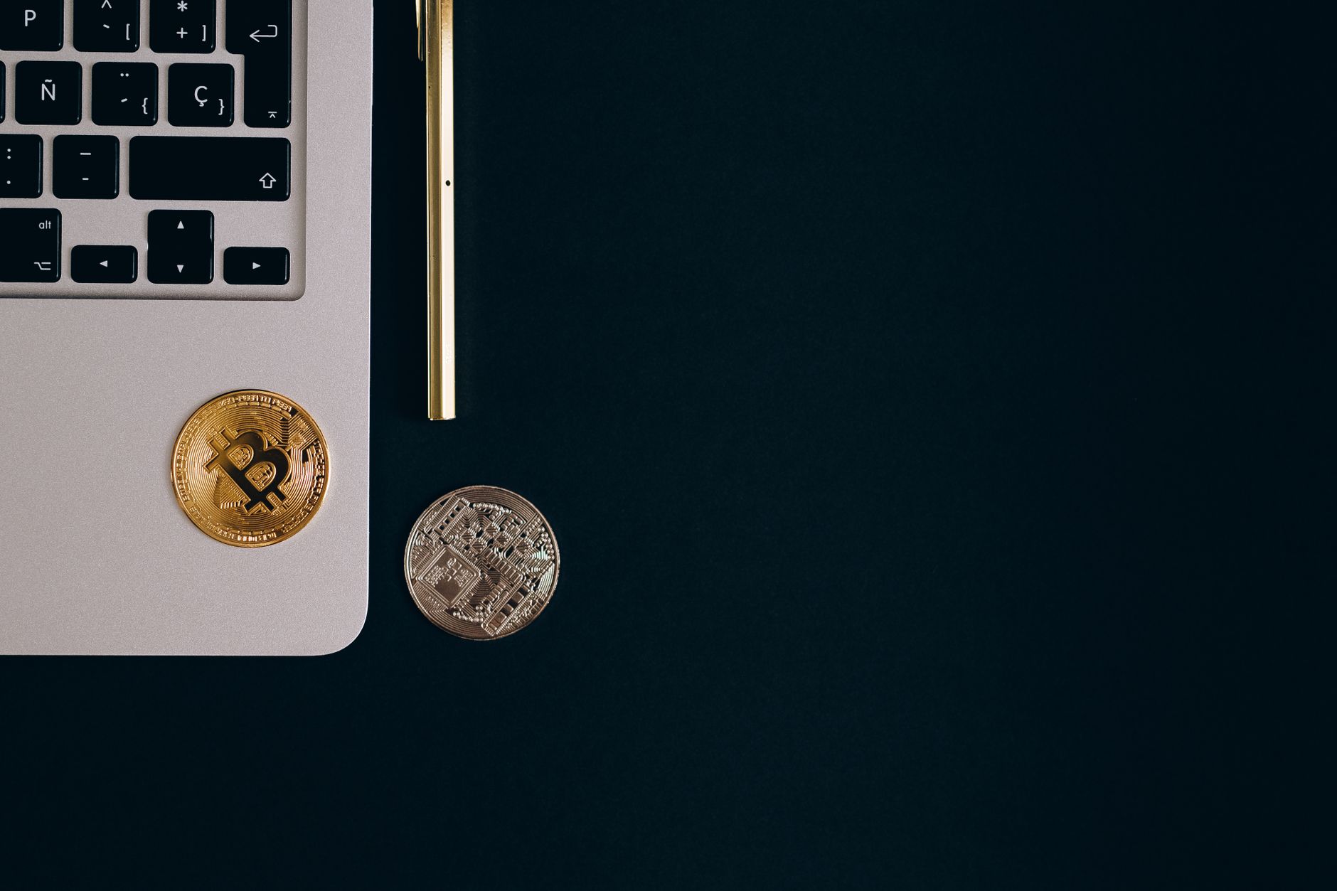 Close-up view of Bitcoin and Ethereum coins next to a laptop and pen on a black surface. — How to Navigate Volatility on Cryp