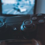 A hand holding a wireless game controller in front of a blurry screen, capturing the gaming experience. — Info Blogs Vs The N