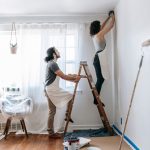 Couple renovating their home, with man supporting ladder and woman working on walls indoors. — Information Inspecting within