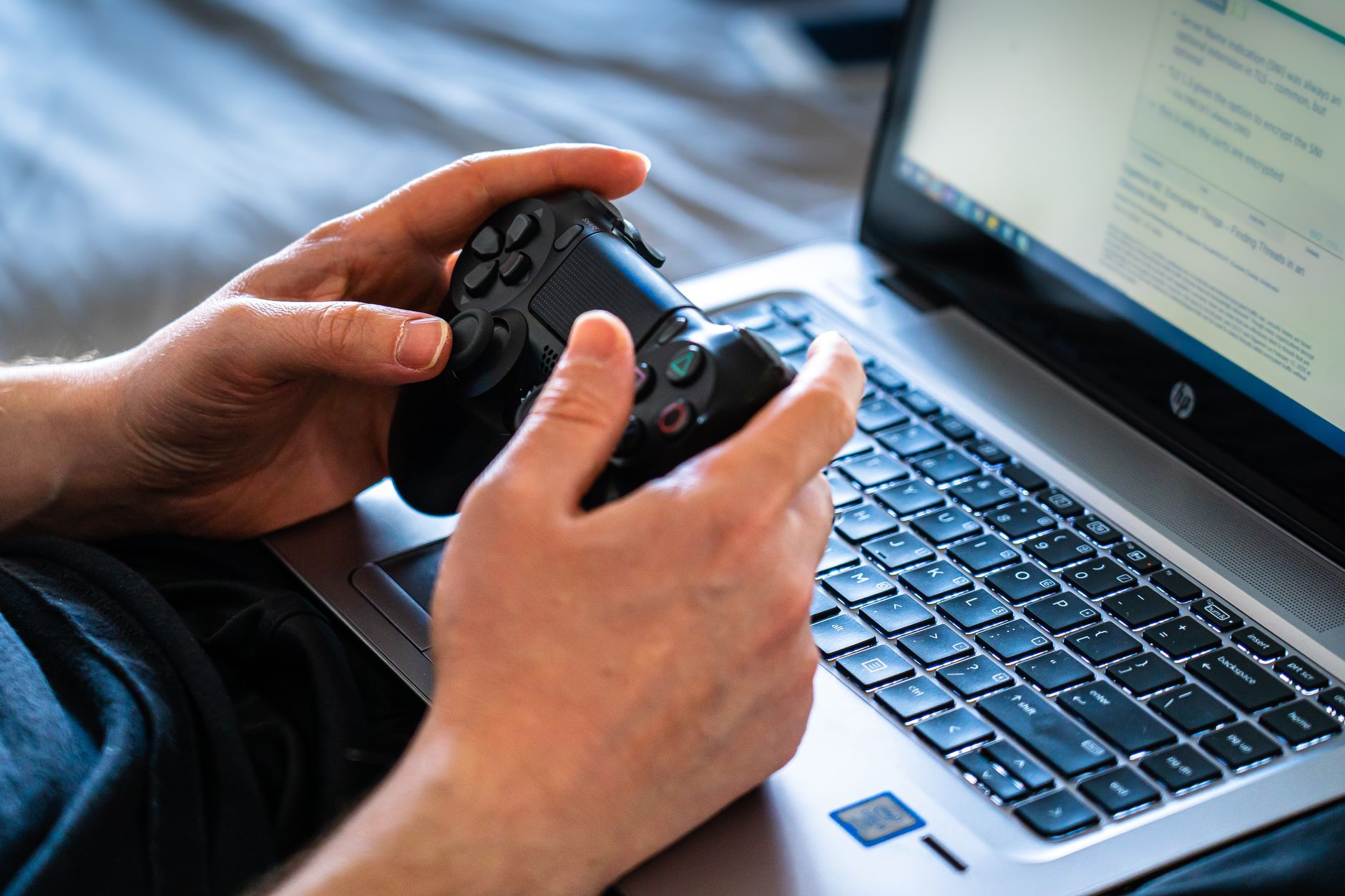 Person holds a gaming controller while interacting with a laptop, emphasizing modern gaming technology. — Information Media I