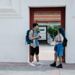 Two young travelers with backpacks share a moment at a cultural landmark, blending contemporary style with tradition. — Plane