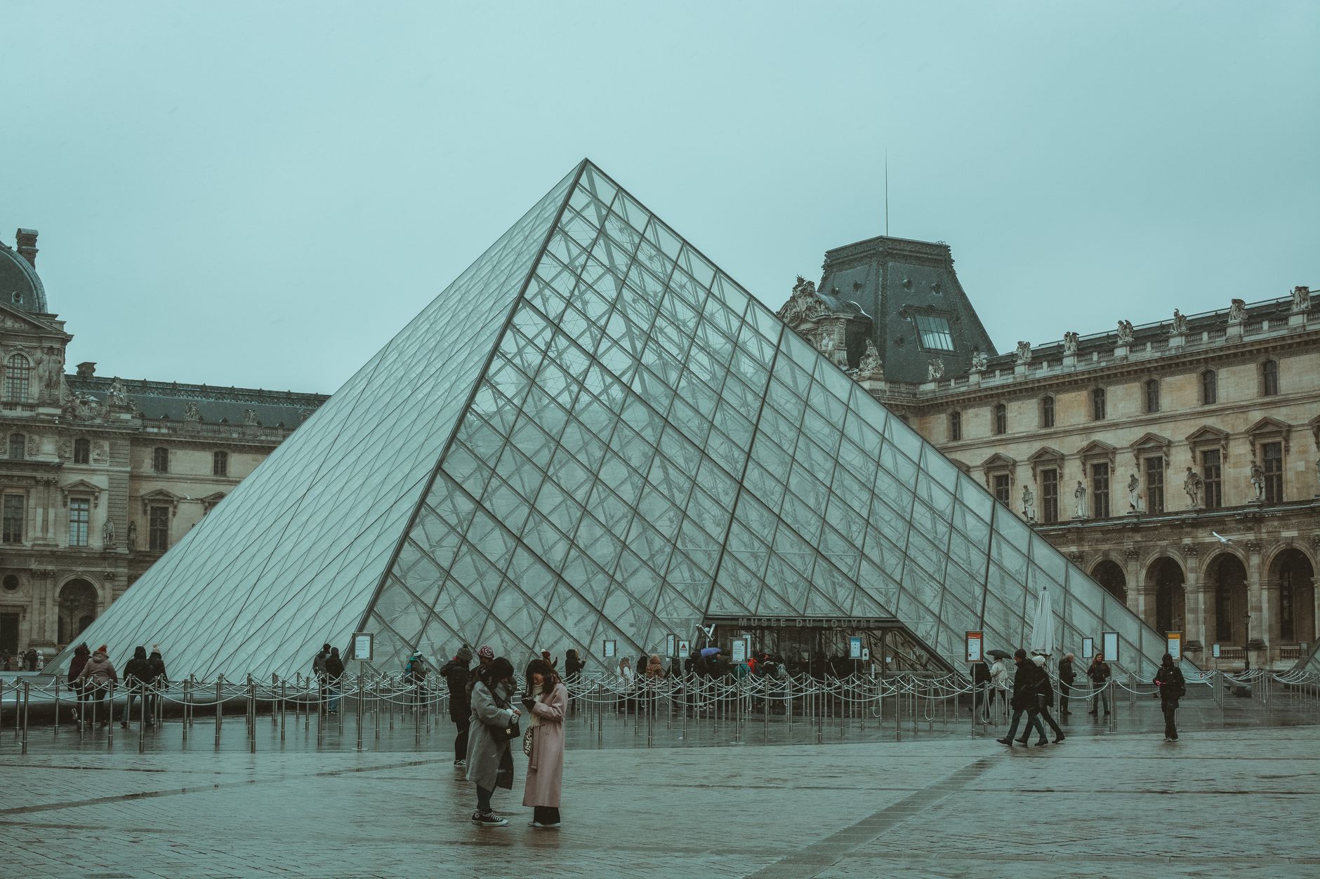 A winter day at the iconic Louvre Museum pyramid in Paris, capturing tourists and the architectural beauty. — Sources for Tre