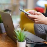A person working on a smartphone and laptop at home with plants nearby. — The Enterprise Design and Current day Monetary syst