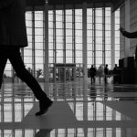 Business professionals walk through a modern, glass-paneled indoor space. — The Future of Medicare Part D: What to Expect in