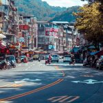 Vibrant urban street scene with shops, vehicles, and mountains in an Asian city. — The Rise of Luxury Property Investments in