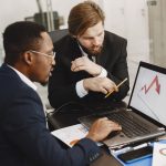 Two business professionals discuss marketing data on a laptop in a modern office. — The UFABET Gambling Advantage: Tips for S