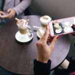 Two women in a cafe capturing photos of their coffee with smartphones. — View Velocity: Supercharge Your Instagram with Purch