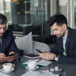Two businessmen in a cafe working on smartphones and laptops, engaged in a meeting. — Well being and health Info These days