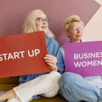 Two women on a sofa holding signs promoting startup and business women. — Why do you need a survival kit- The importance